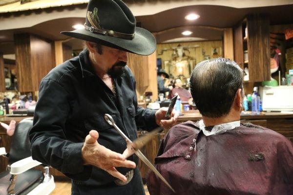 An old cowboy gets a wooden ball placed inside his cheek to spread out the skin for a clean shave