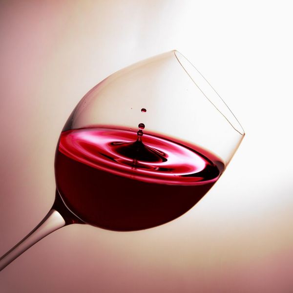 A tipped glass of red wine with a white and red-hued background.