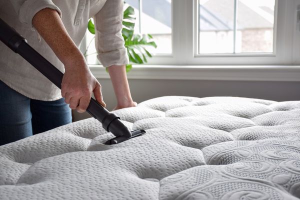 Woman using a vacuum cleaner to vacuum a mattress in a bedroom.